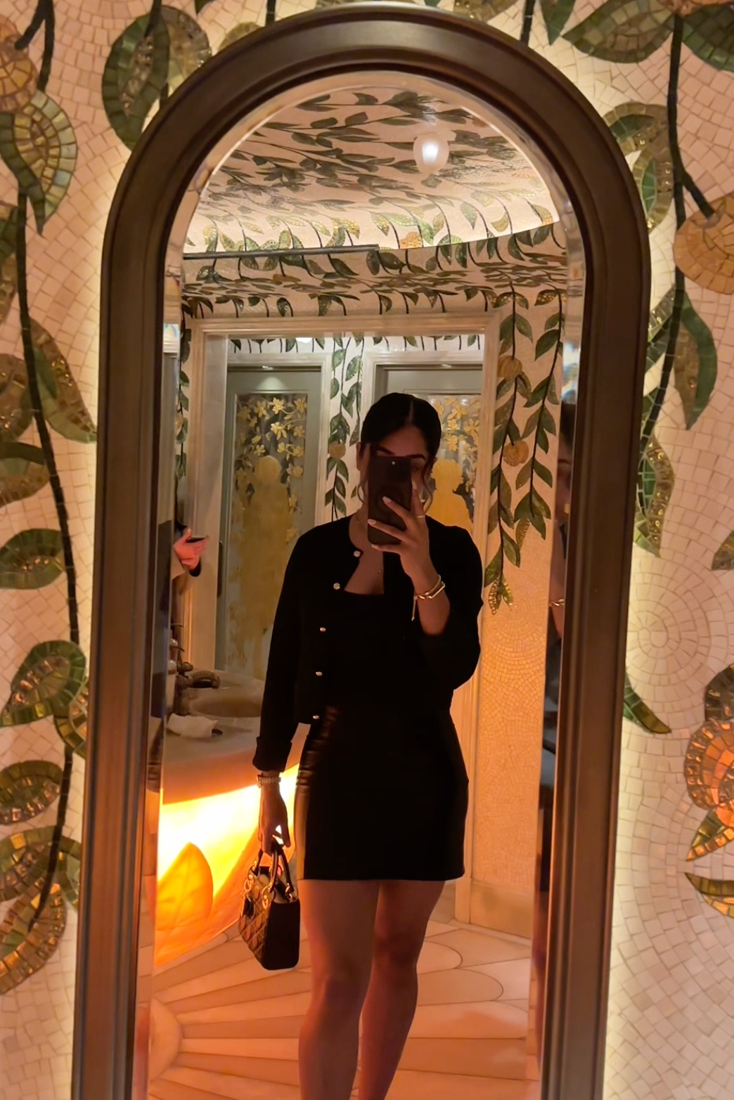 Person taking a mirror selfie in a room with floral wallpaper